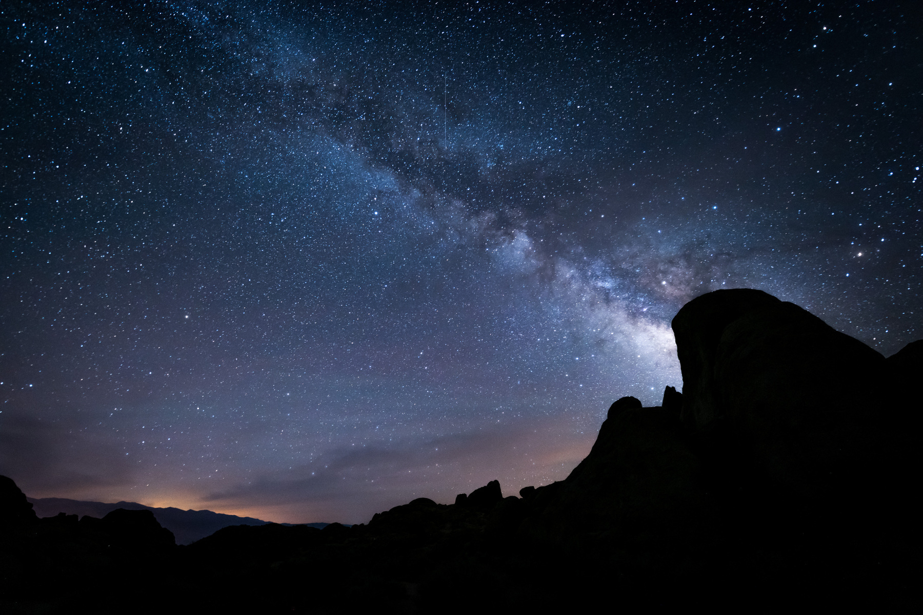 Auto-generated description: A star-filled night sky showcases the Milky Way galaxy above silhouetted rock formations.