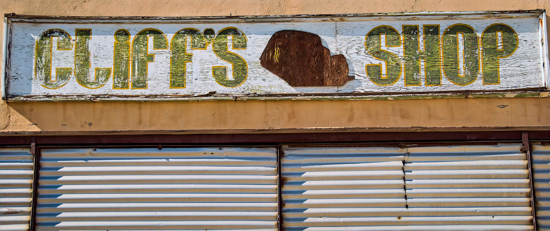 A weathered sign reading CLIFF'S SHOP with a faded silhouette above corrugated metal blinds.