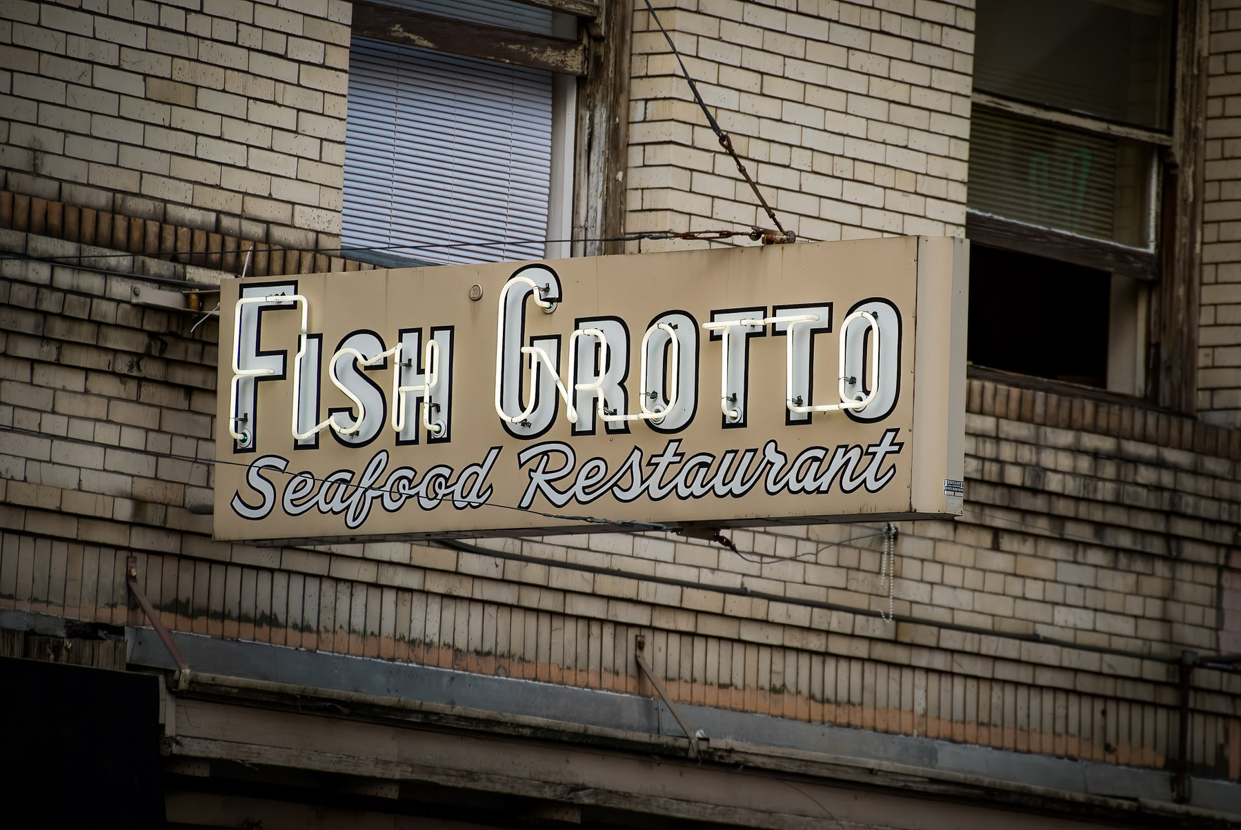 A sign displays Fish Grotto Seafood Restaurant against a brick wall background.