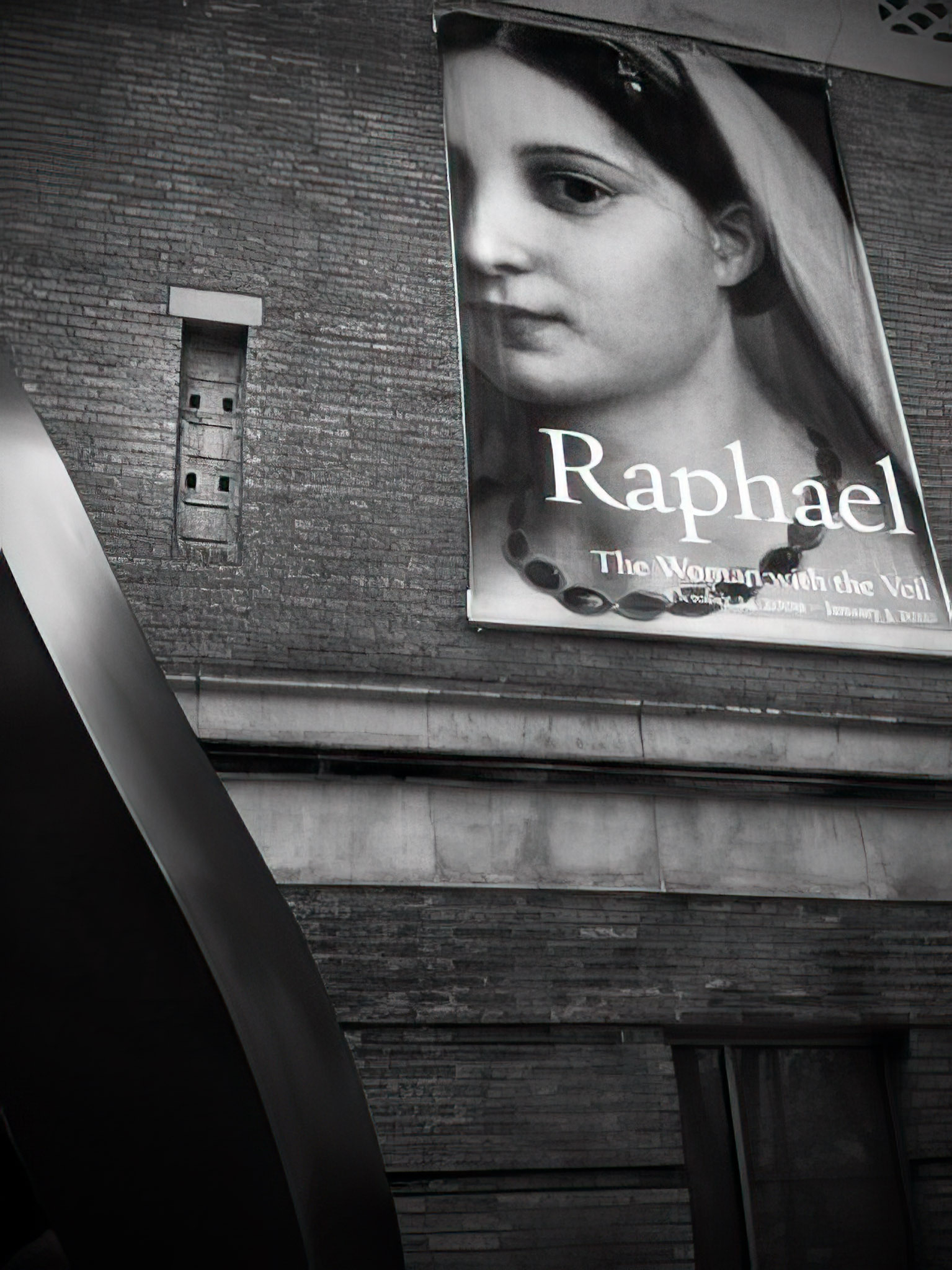 A large poster featuring a partial view of a woman's face and the text Raphael is displayed on a brick wall.