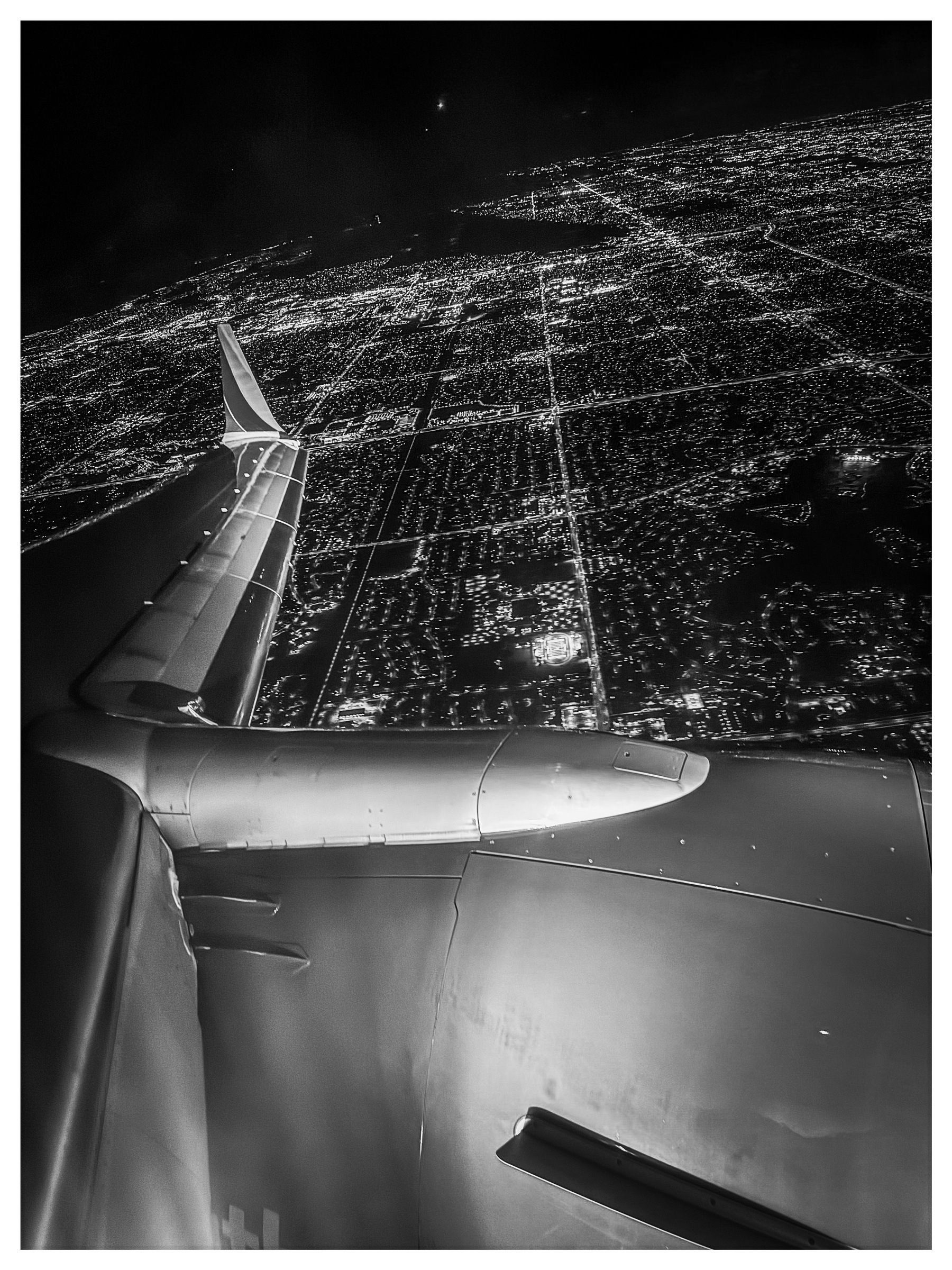 Auto-generated description: An airplane wing is visible against the illuminated grid-like cityscape at night.