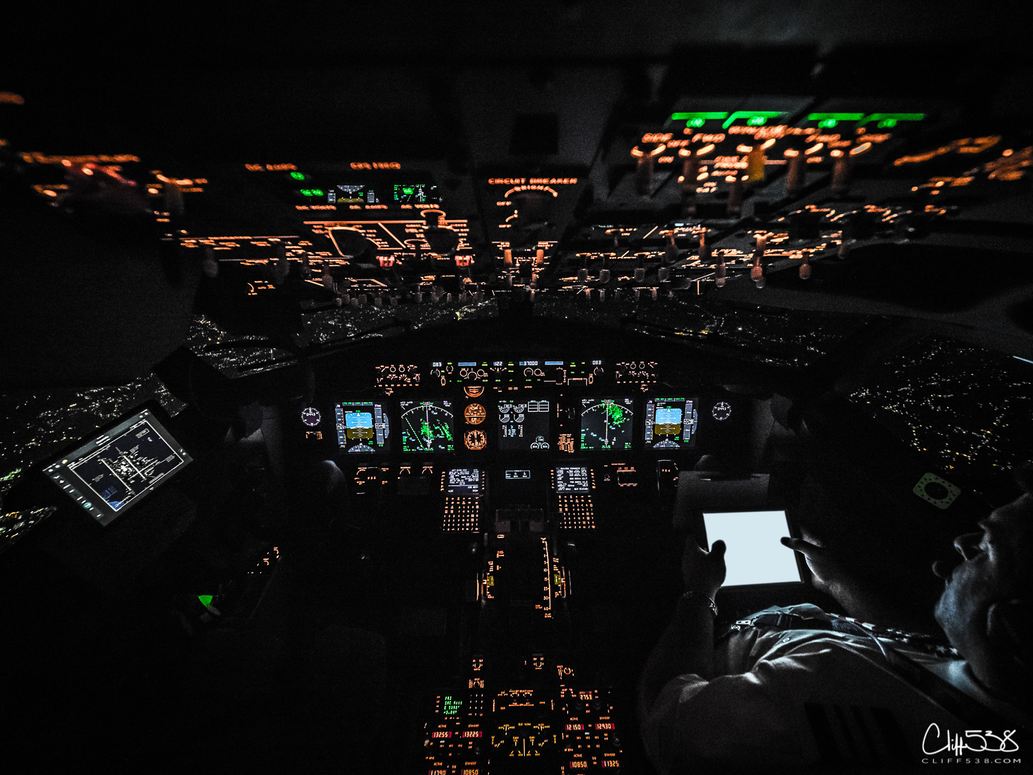 Auto-generated description: A dimly lit airplane cockpit at night with illuminated controls and a pilot engaged in flight operations.