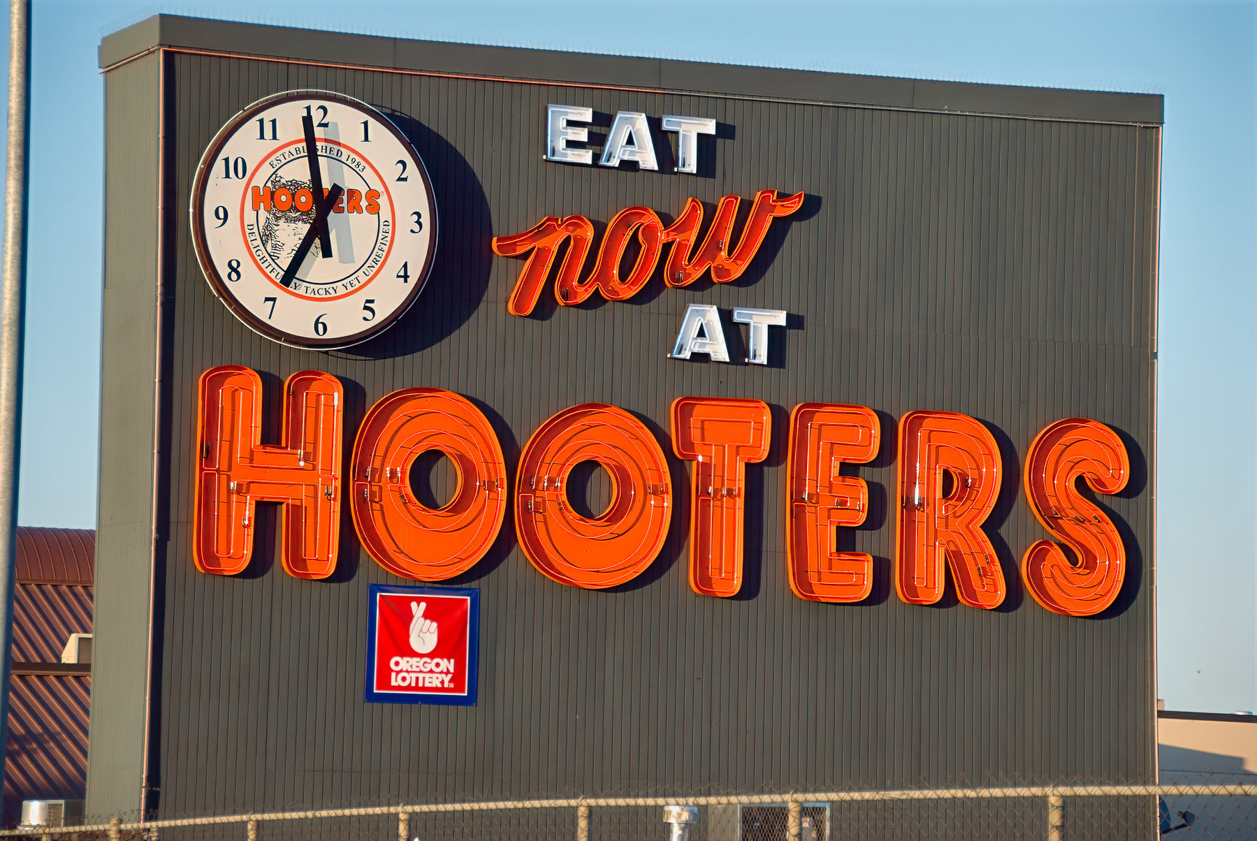 A large sign advertising Hooters features a clock and the phrase Eat now at Hooters, along with the Oregon Lottery logo.