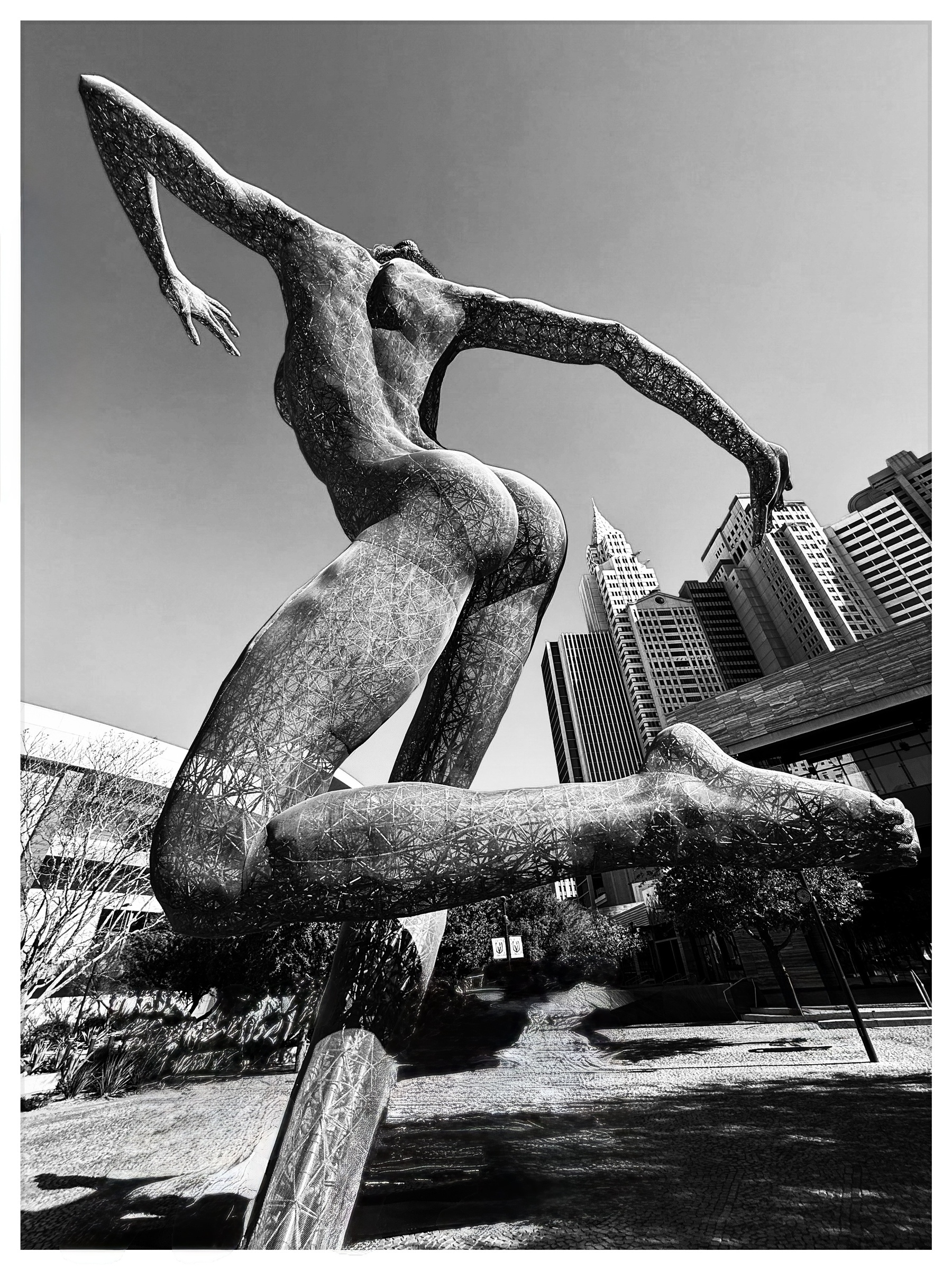 Auto-generated description: A dynamic sculpture of a human figure in mid-leap is set against a backdrop of modern skyscrapers.