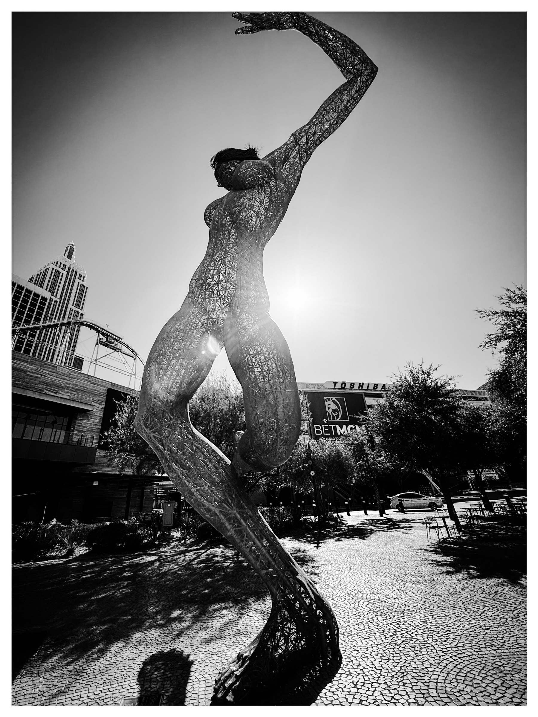 Auto-generated description: A towering, intricate metal sculpture of a dancing figure is silhouetted against the sun in an urban setting.