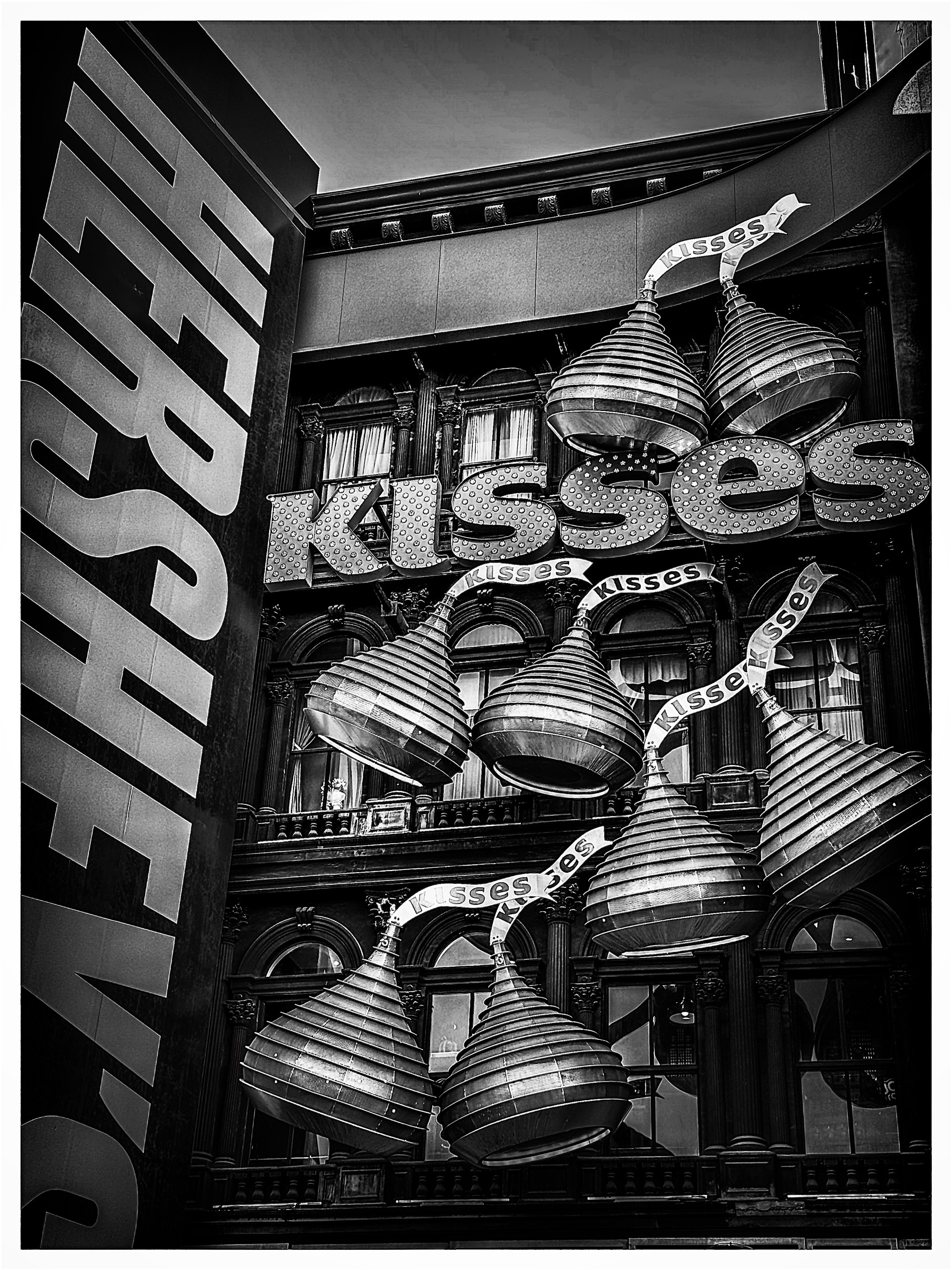 Auto-generated description: Large, metallic Hershey's Kisses are displayed in front of a building with illuminated signage.