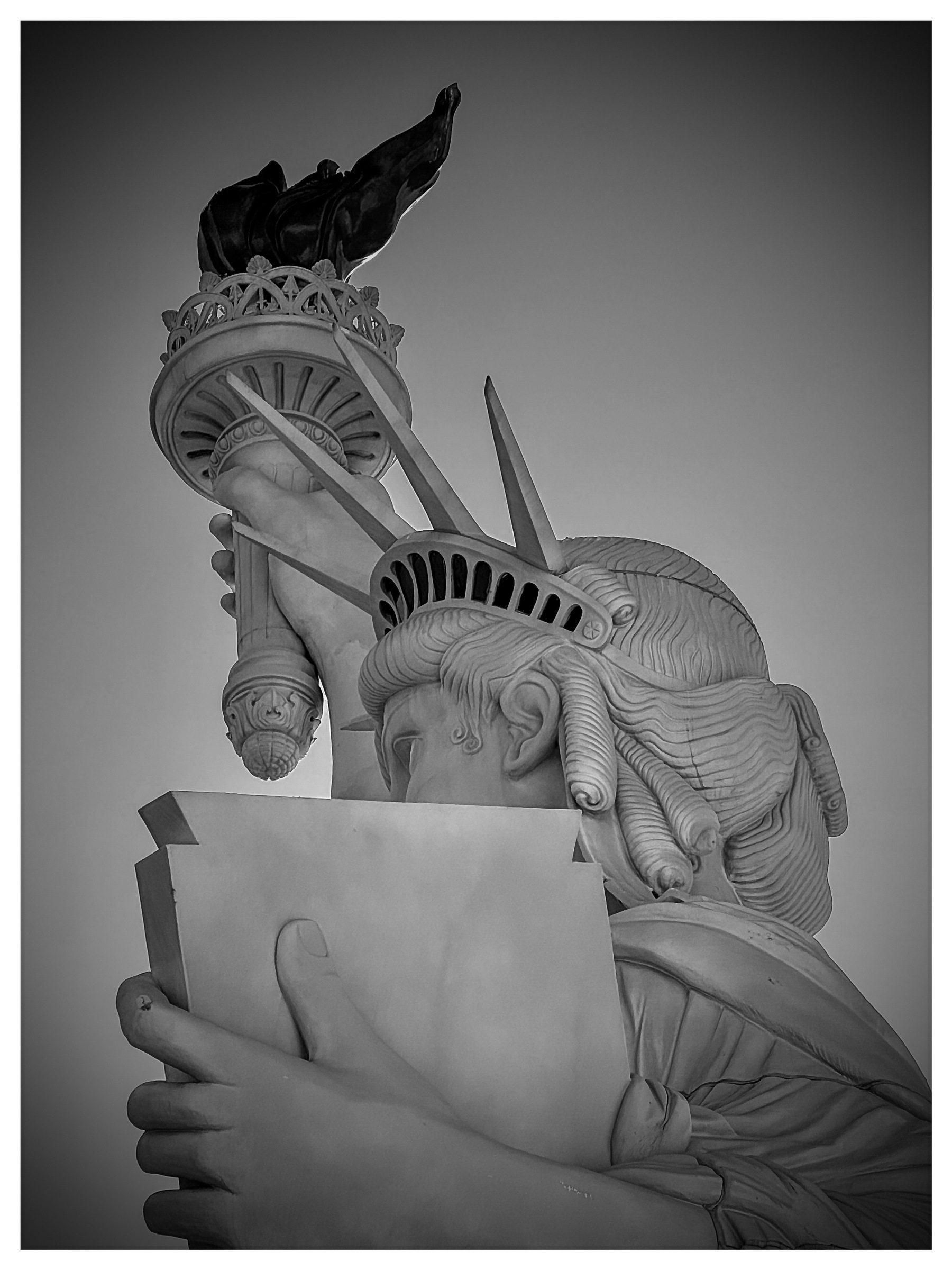 Auto-generated description: A grayscale close-up of the Statue of Liberty, focusing on the torch and upper portion with a slightly tilted perspective.