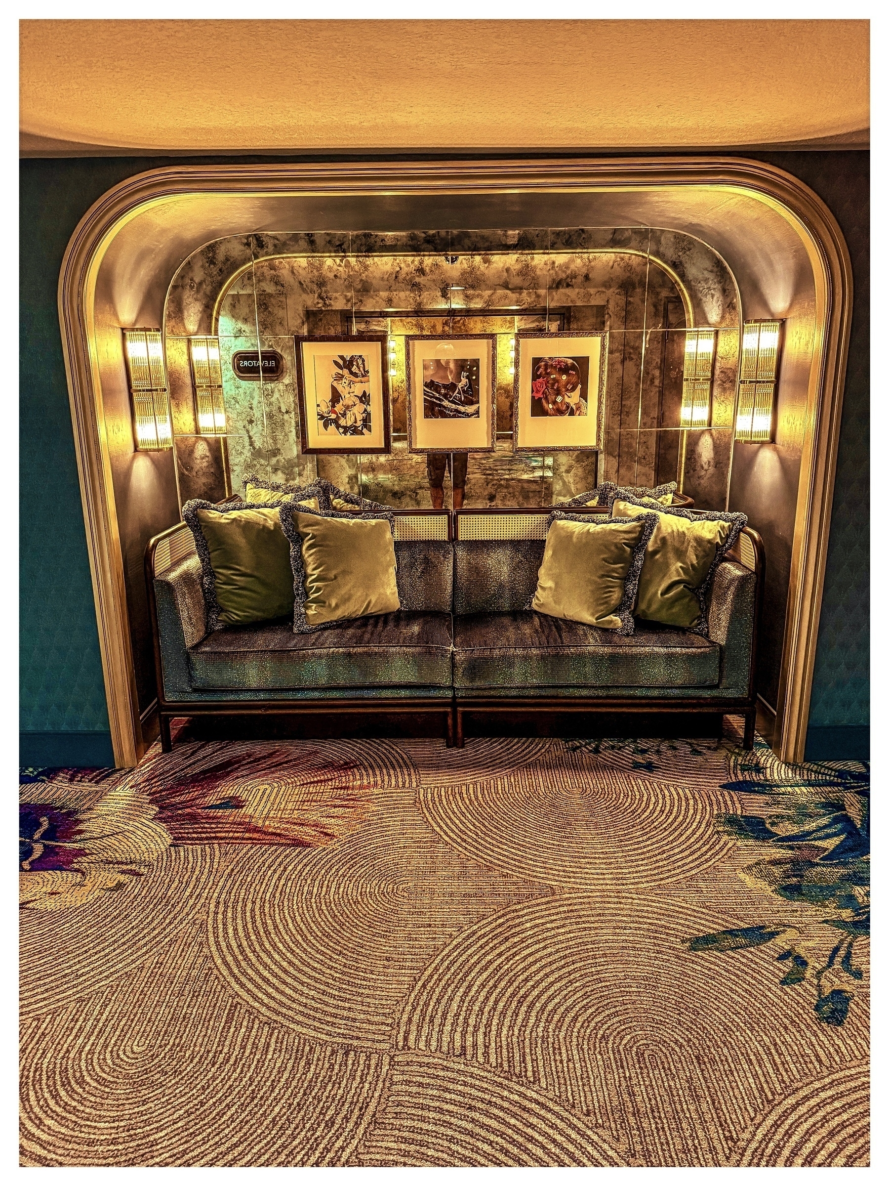 Auto-generated description: A cozy, ornately decorated seating alcove features a cushioned bench with throw pillows, framed artworks, and warm lighting.