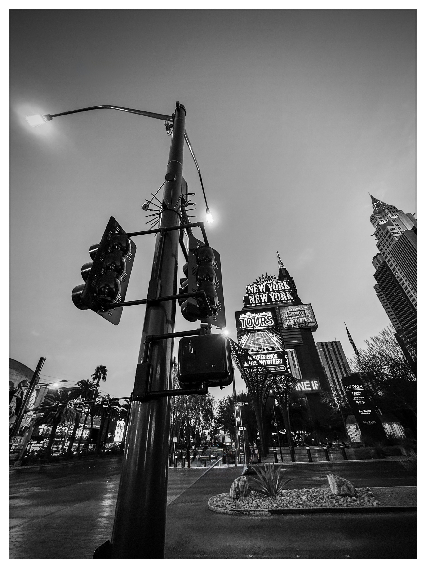 Auto-generated description: A black and white street-level view showcases a traffic light and the iconic New York, New York hotel signage in Las Vegas against a dusky sky.