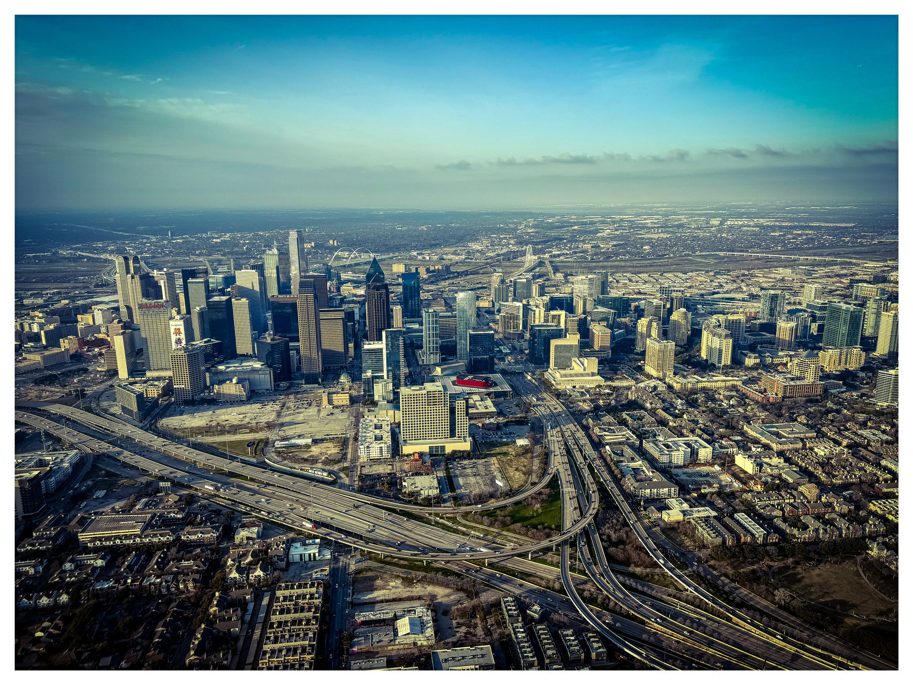 Auto-generated description: An aerial view showcases a sprawling urban skyline with dense clusters of skyscrapers and a network of highways.