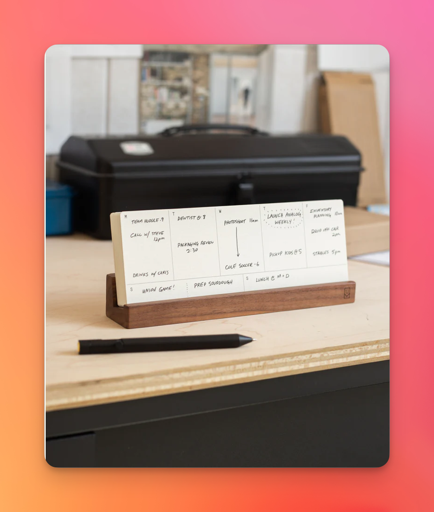 Auto-generated description: A desk planner with a pen is placed on a table in front of a black briefcase.